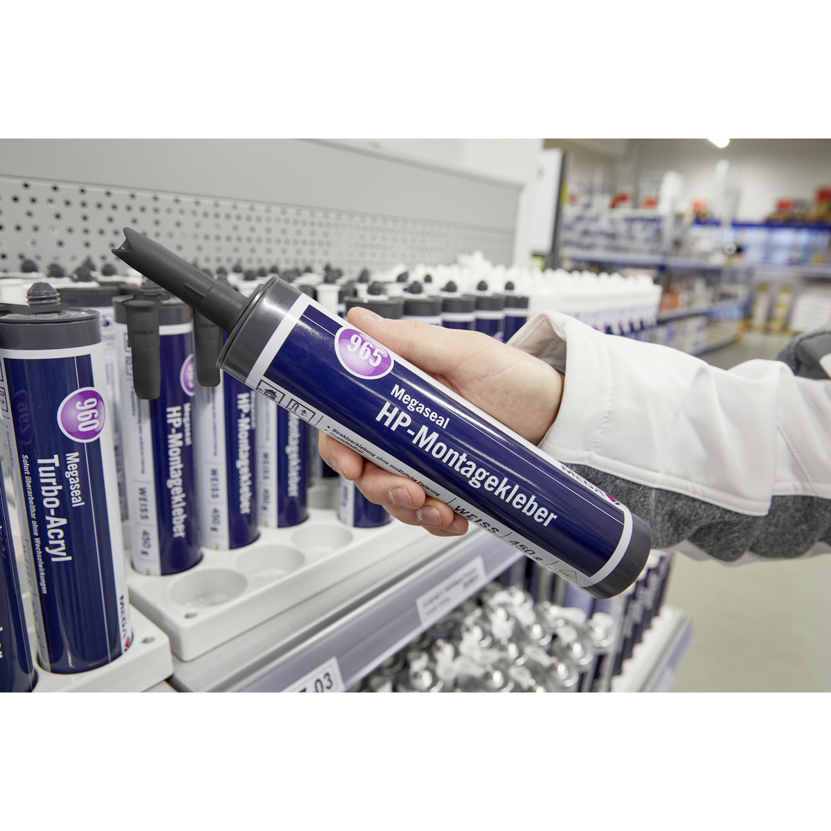 Hand hält eine Kartusche Megaseal HP-Montagekleber in einem Baumarktregal