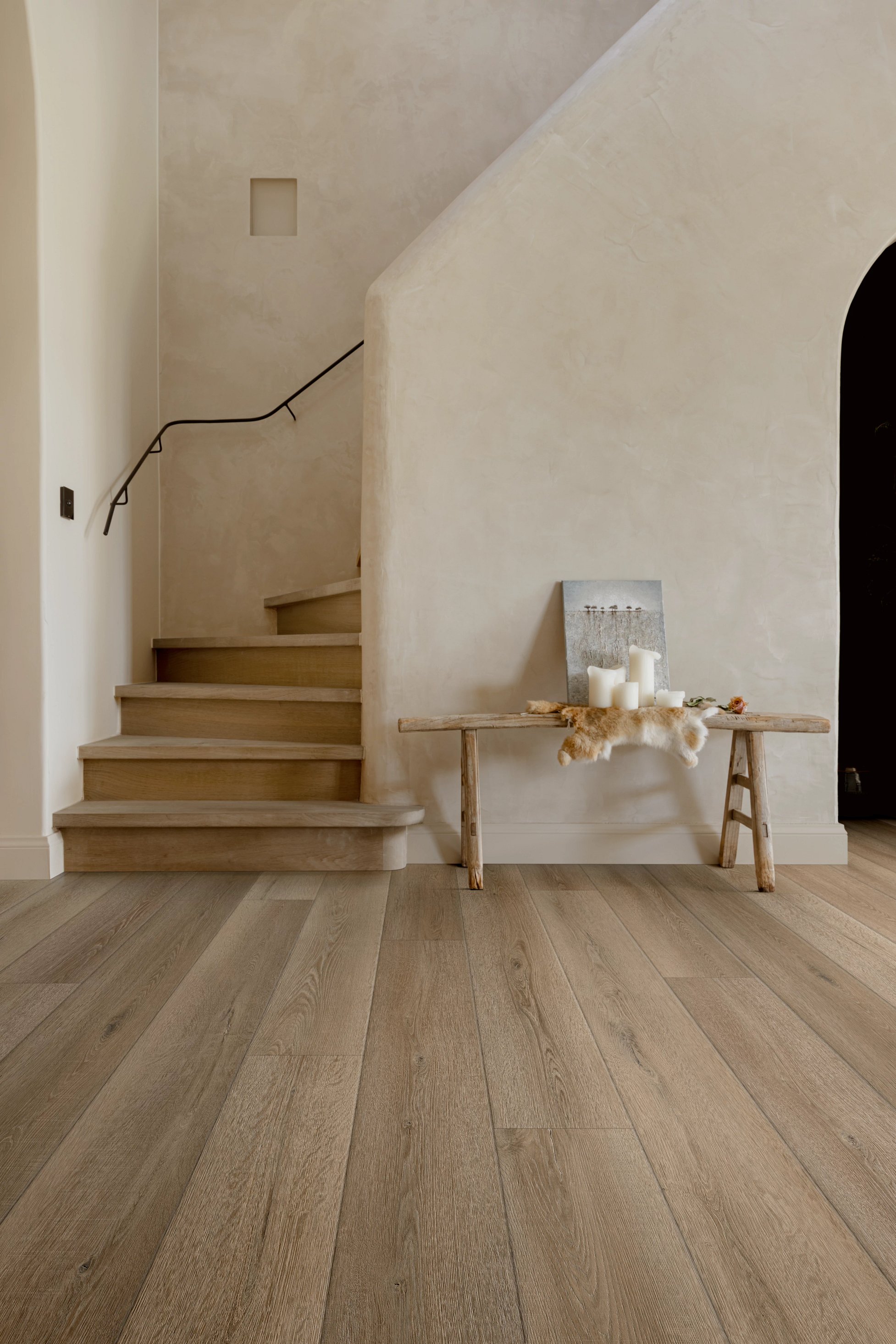 Ein stilvolles Treppenhaus mit Holztreppe, heller Wand und rustikalem Tisch mit Kerzen und Dekoration.