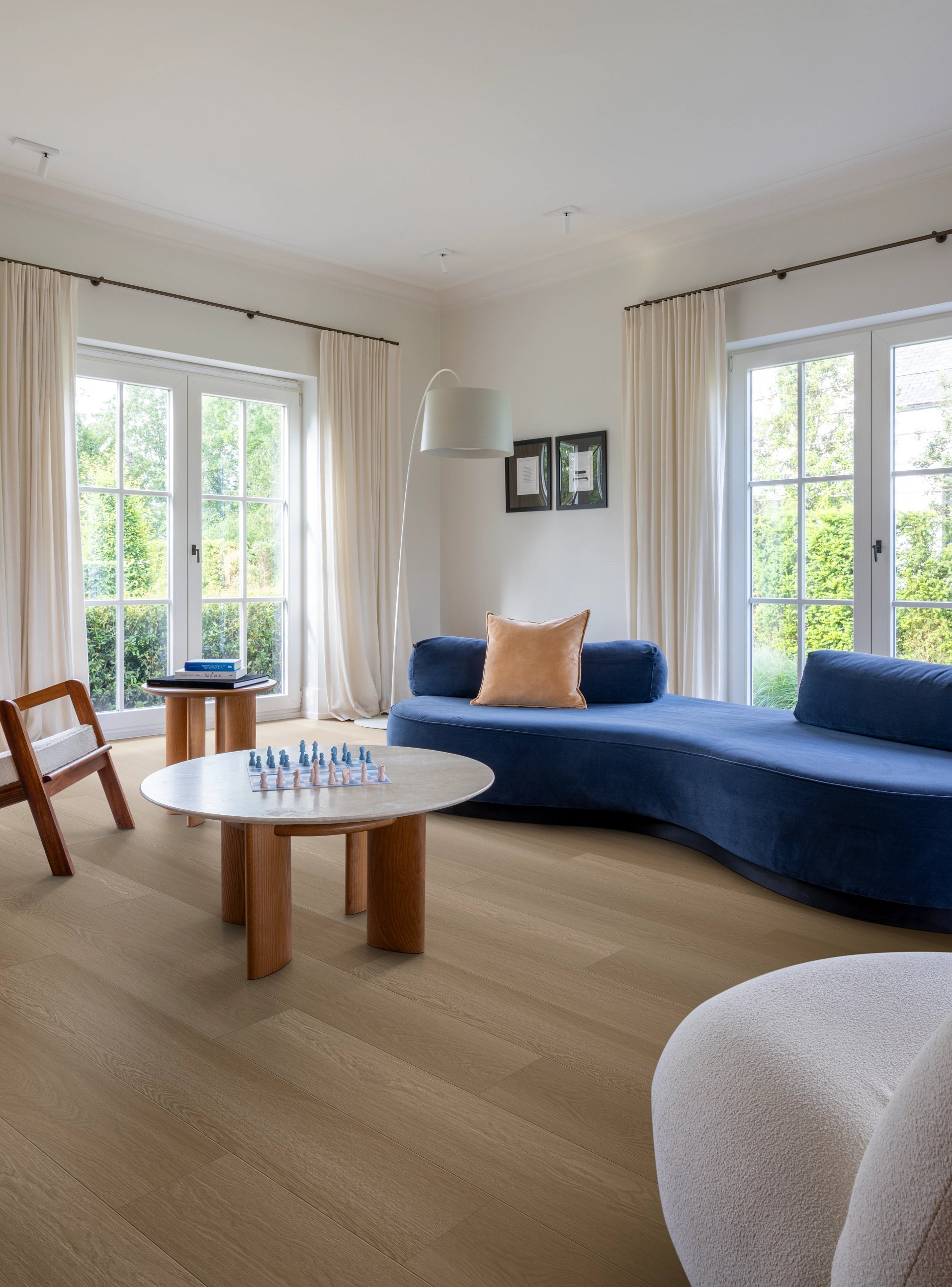 Modernes Wohnzimmer mit blauer Sofa-Landschaft, rundem Marmortisch und großen Fenstern mit weißen Vorhängen