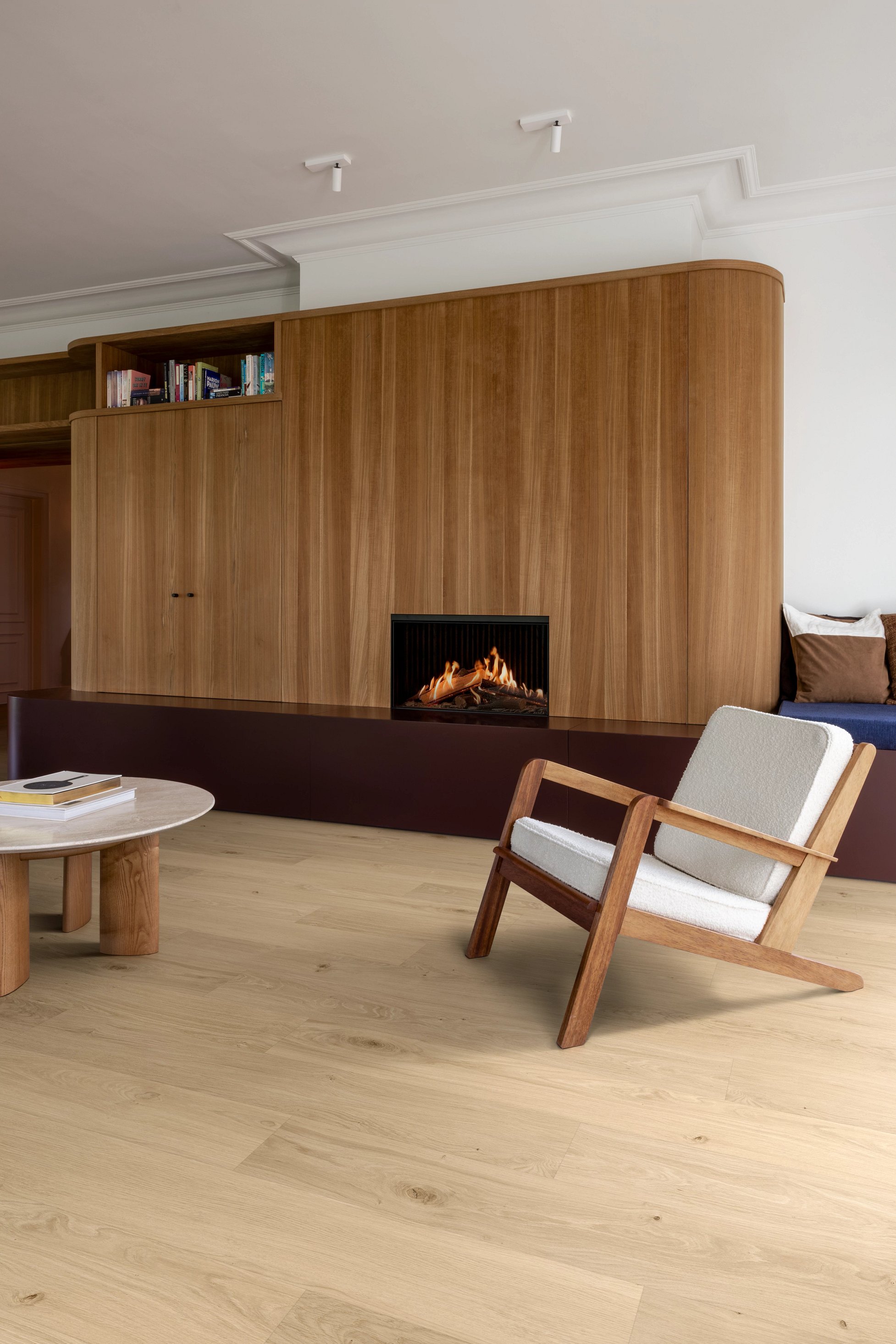 Wohnzimmer mit Kamin, Holzwänden, beigem Sessel und rundem Holztisch