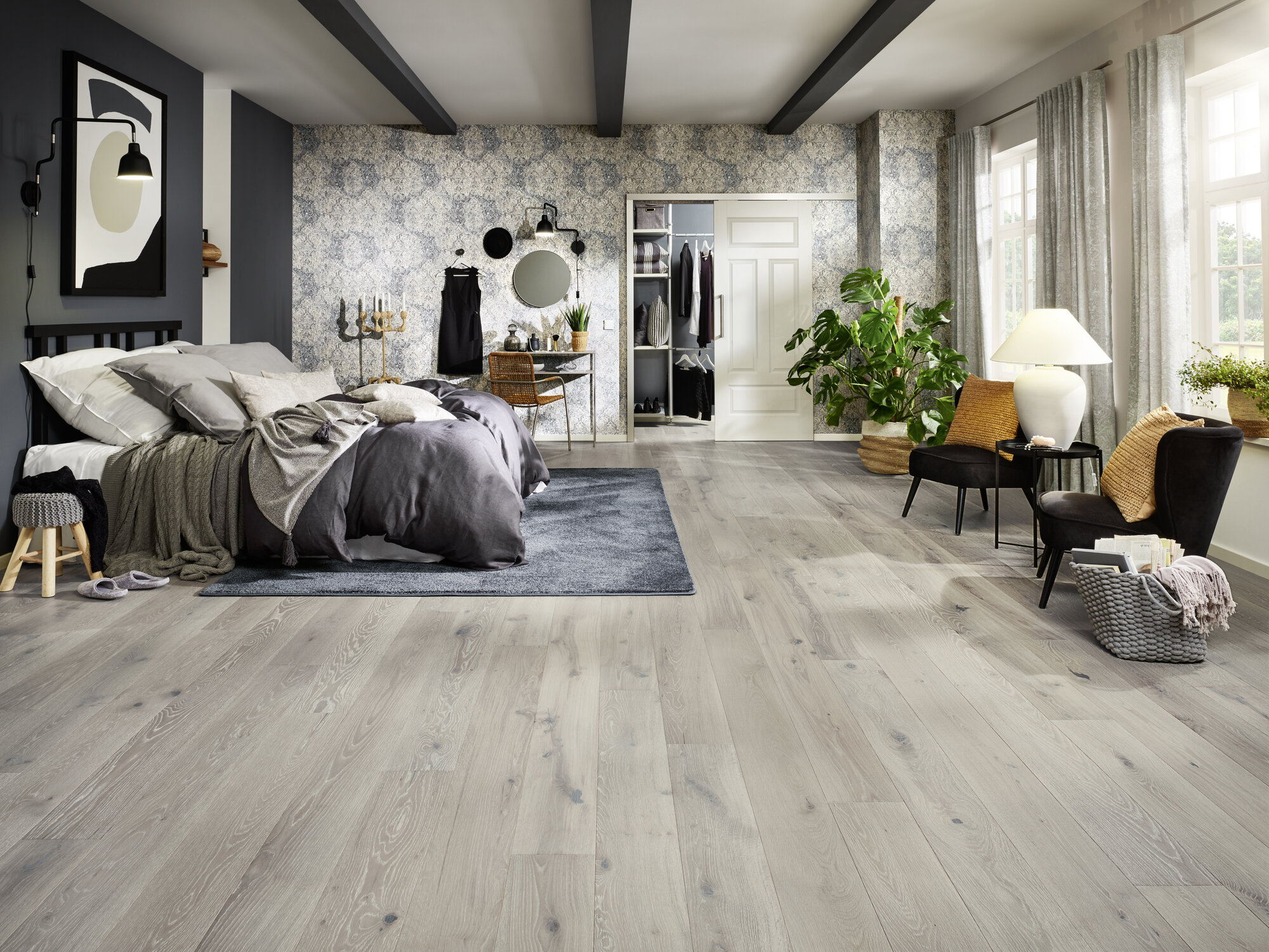 Gemütliches und modern eingerichtetes Schlafzimmer mit Laminatboden, Doppelbett, Teppich, Pflanzen und Sitzbereich.